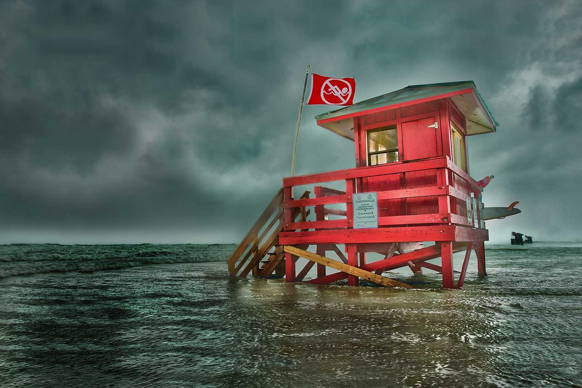 Red lifeguard tower surrounded by surf beneath storm clouds
